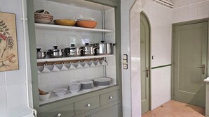 Una cocina con paredes de azulejos blancos, una puerta verde y estantes con ollas, sartenes y tazas blancas.