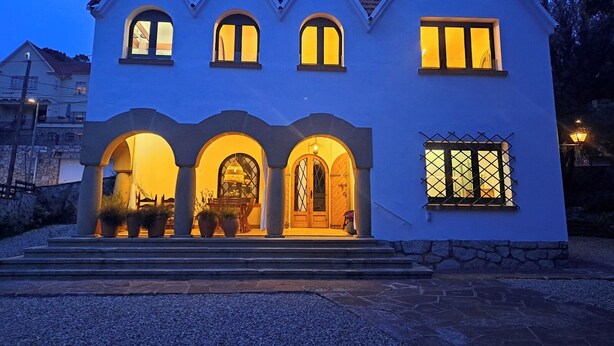 Una casa de dos pisos con fachada simétrica, múltiples ventanas y una entrada central con arco.