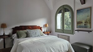 Un dormitorio con cama de madera, dos lámparas de noche, un ventanal con vistas a zonas verdes y un cartel en la pared.