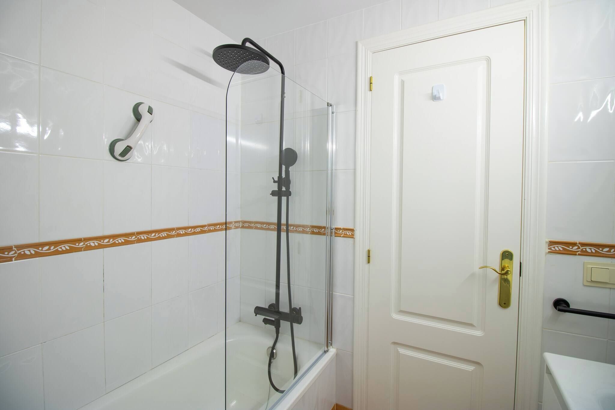 A bathroom with a glass-enclosed shower, a white door with a brass handle, and a towel rack on the wall.