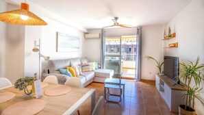 A modern living room with a sofa, dining table, and TV stand. - Penthouse Kalymnos (Platja de L'arenal)