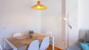 A dining area with a wooden table, white chairs, a hanging lamp, and a floor lamp. - Penthouse Kalymnos (Platja de L'arenal)