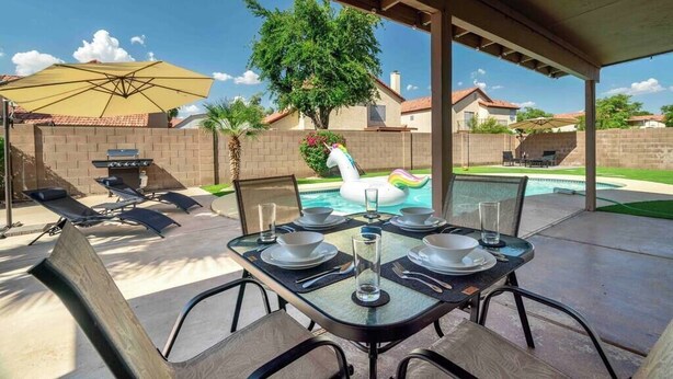 Une terrasse extérieure avec une table dressée pour quatre personnes, une piscine agrémentée d’un cygne gonflable et, au fond, un barbecue.