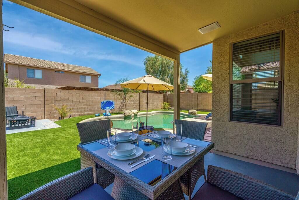 A patio with a table set for dining, overlooking a swimming pool and a backyard.
