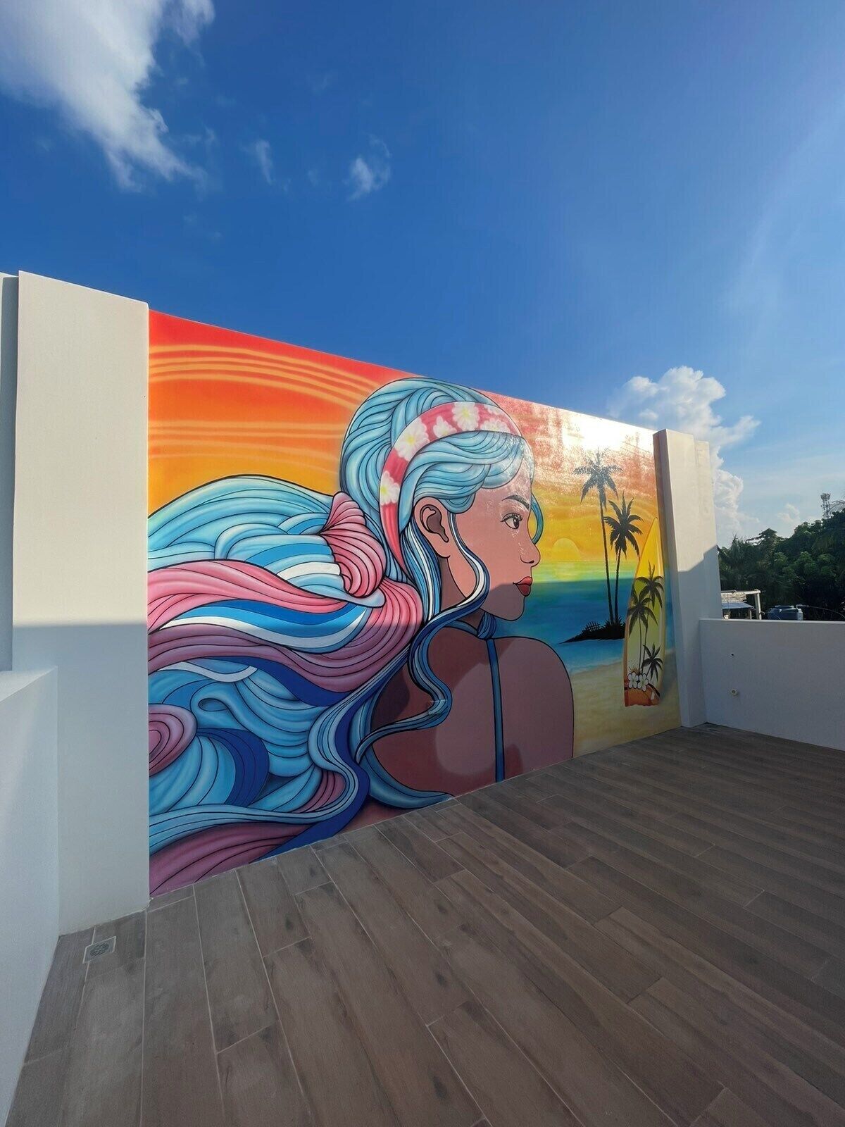 A mural of a woman with flowing hair against a sunset background, depicting a beach scene with palm trees.