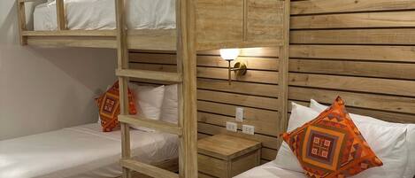 A bunk bed room with wooden slats on the wall, a bedside table with a lamp, and two orange patterned pillows.