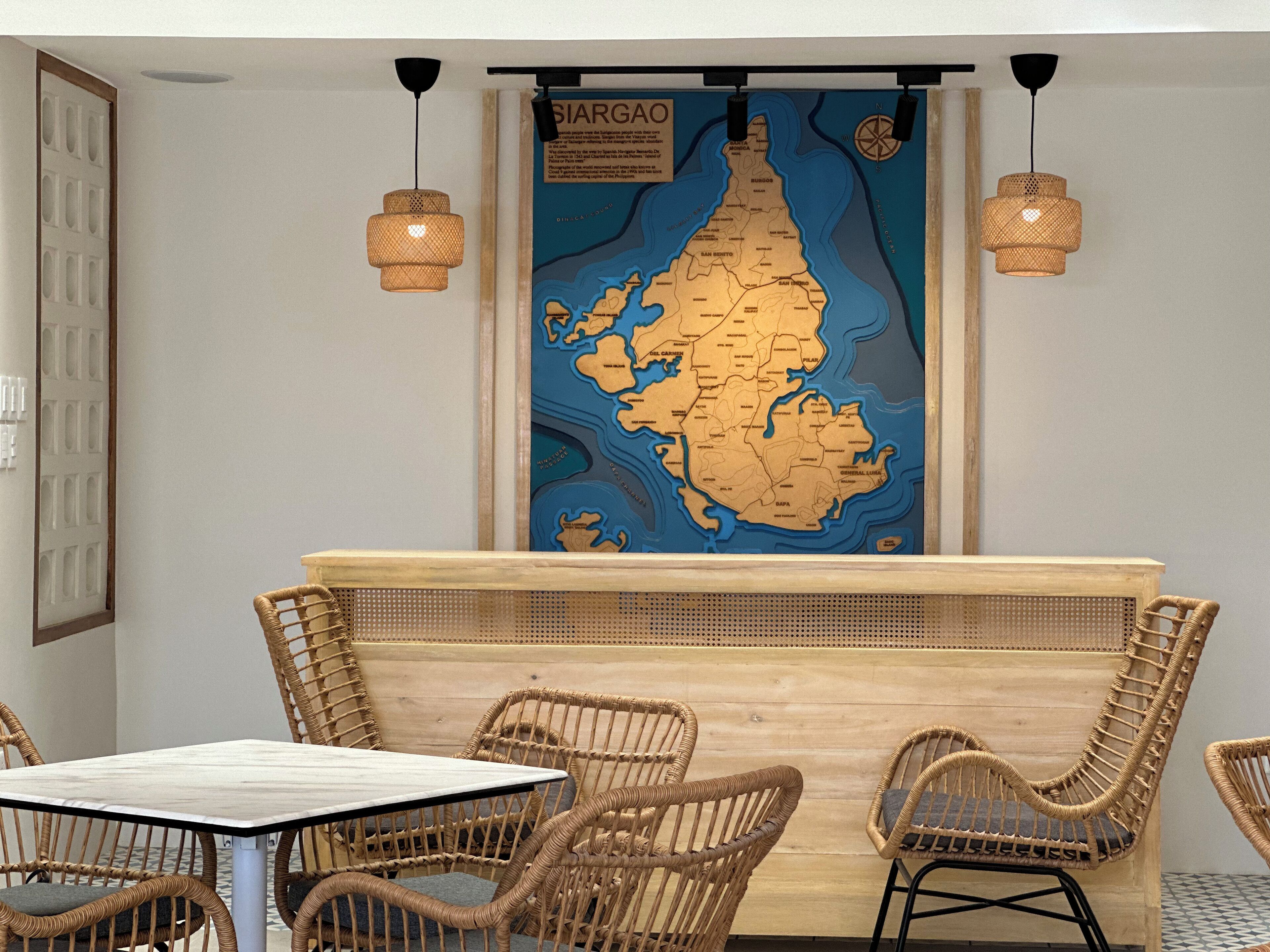 A restaurant interior with wicker furniture, a wooden counter, and a map of Siargao on the wall.