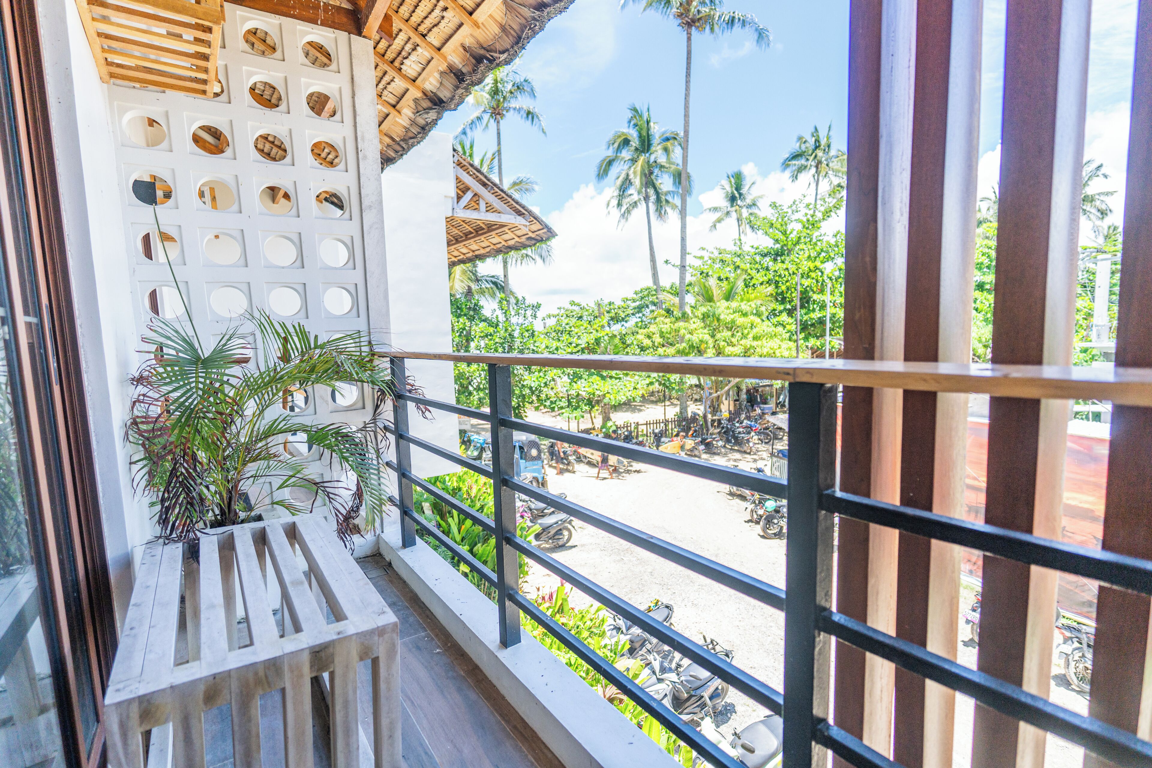 A balcony with a view of a street, palm trees, and parked motorcycles.