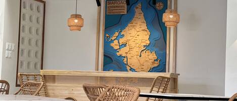 A restaurant interior with wicker chairs, a map of Siargao, and hanging pendant lights.