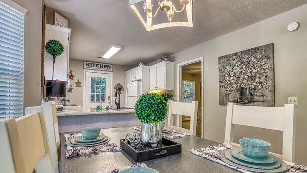 A modern kitchen with white cabinets, a chandelier, and a dining area with blue bowls and a decorative tree centerpiece. - Convenient to Dollywood-Dinner Shows Two Bedroom Two Bathroom- Internet Access (Pigeon Forge)