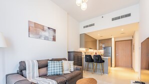 A modern living room with a sofa, two small tables, and a kitchen area visible in the background. - Luxury Meydan Escape Condo with City View (Dubai)