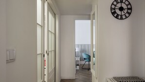 A hallway with a white door, a black wall clock, and a patterned bench.