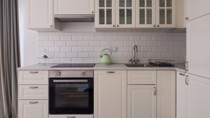 A kitchen with white cabinets, a built-in oven, a green kettle, and a sink with a faucet.