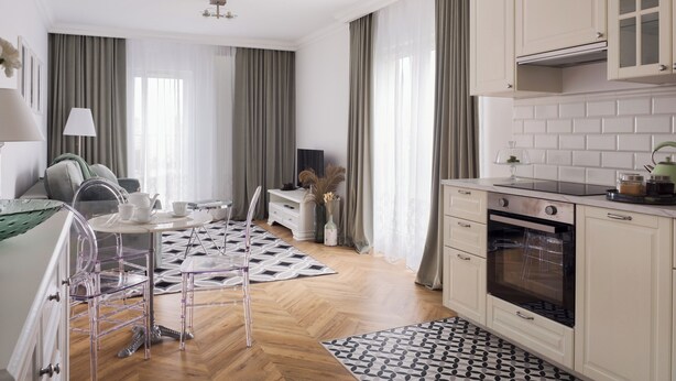 A modern kitchen with white cabinets, a built-in oven, and a dining area with a patterned rug.