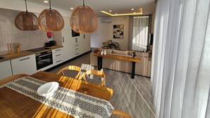 A modern kitchen with white cabinets, a wooden countertop, and a dining area with a wooden table and chairs. - NEXT HOUSE, FURNAS, Vila center (Furnas)