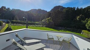 A modern outdoor terrace with a view of a lush garden and hills. - NEXT HOUSE, FURNAS, Vila center (Furnas)