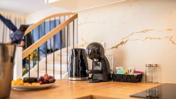 A kitchen with a coffee maker, a kettle, a plate of fruit, and a basket of keys on the counter.