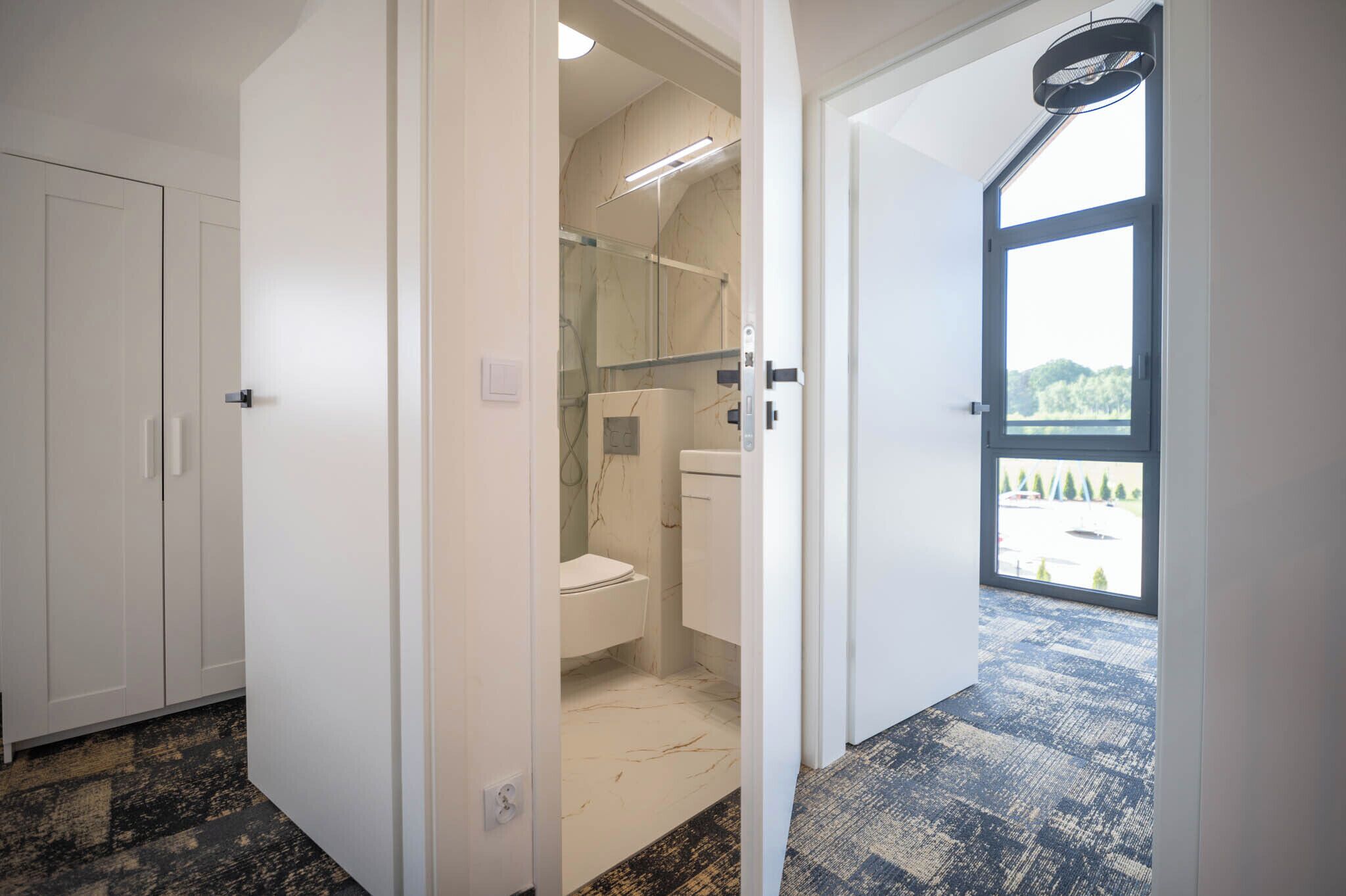 A modern bathroom with a toilet, shower, and a view of a parking lot through a large window.