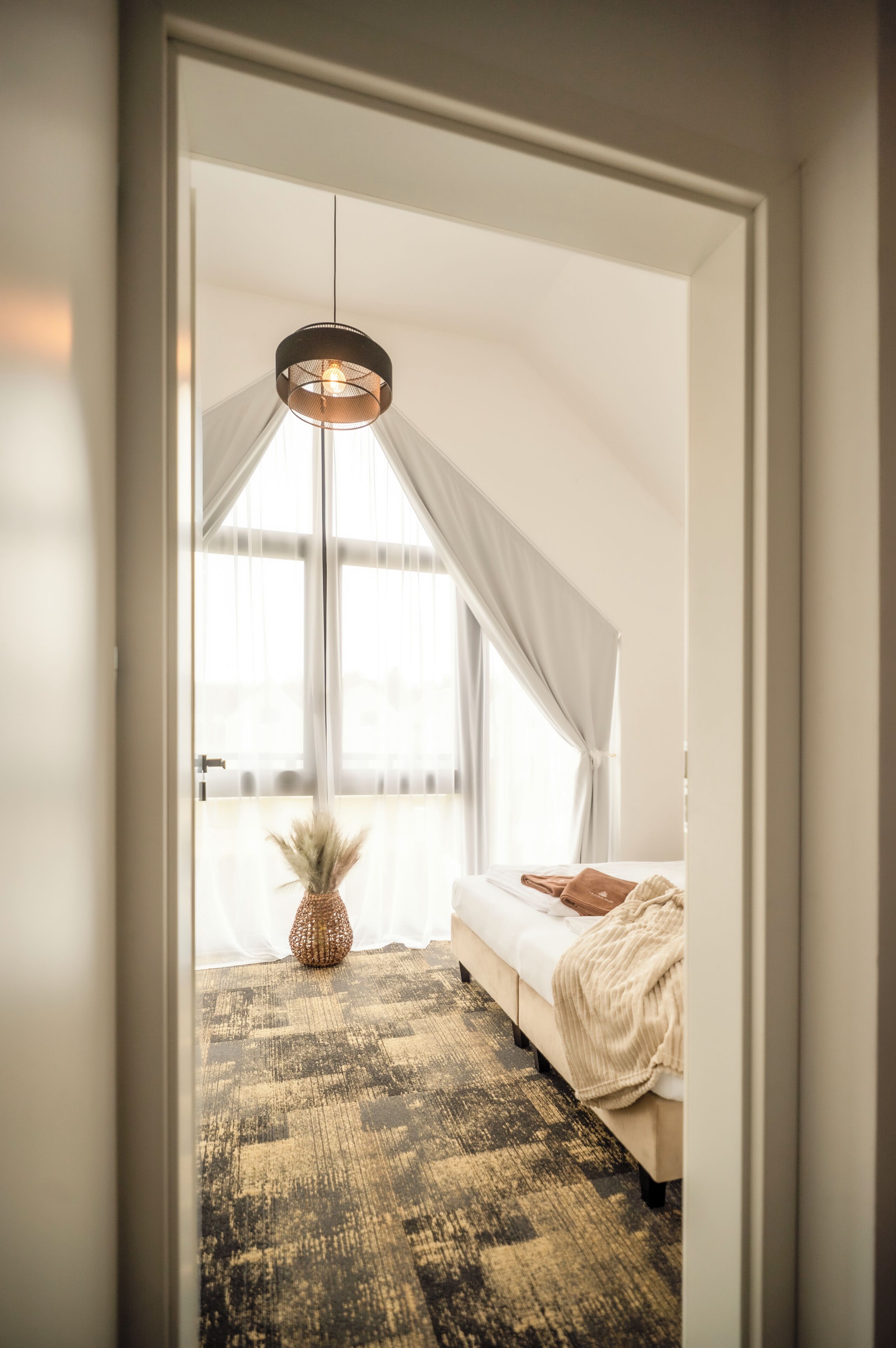 Une chambre à coucher avec un lit, un luminaire suspendu, une fenêtre avec des rideaux et un tapis à motifs.