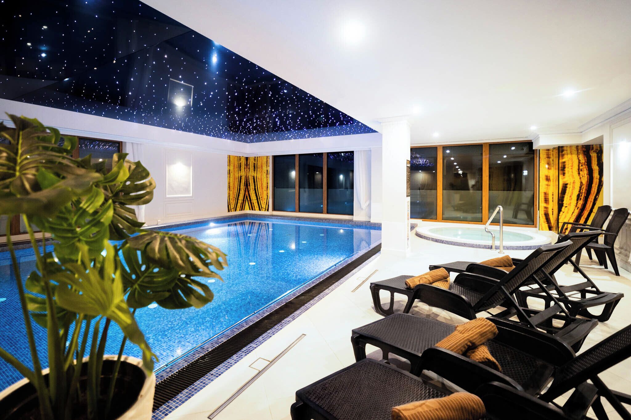 Una piscina interior con techo estrellado, sillones de descanso y un jacuzzi.