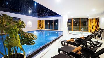 Una piscina interior con techo estrellado, sillones de descanso y un jacuzzi.