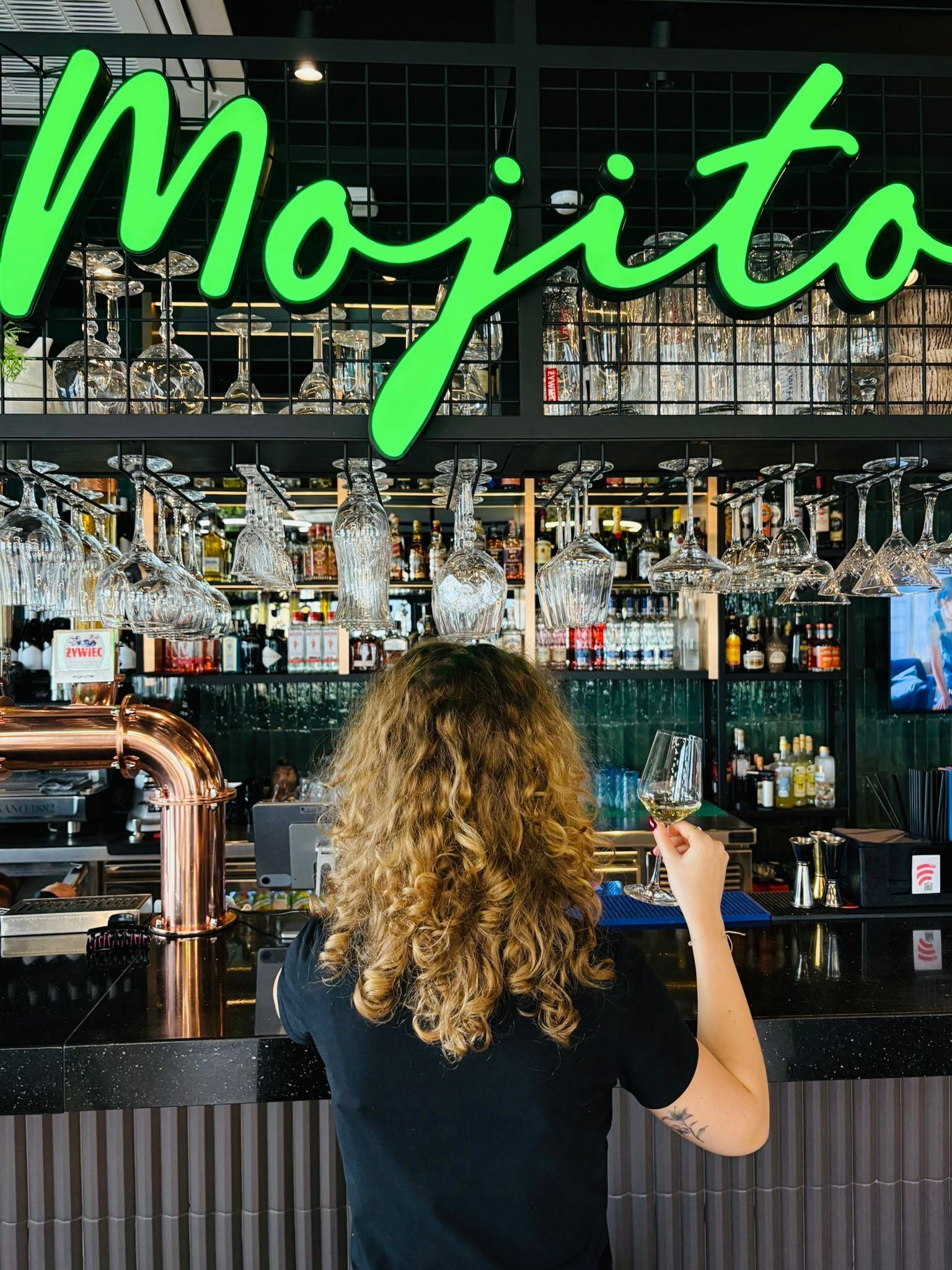 A bar area with a 'Mojito' sign, copper pipes, and various glassware.