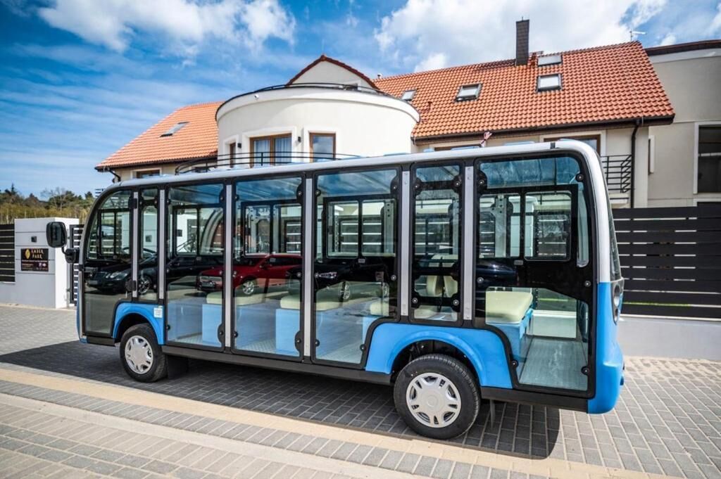 A modern bus parked in front of a building with a tiled roof and a circular white structure.