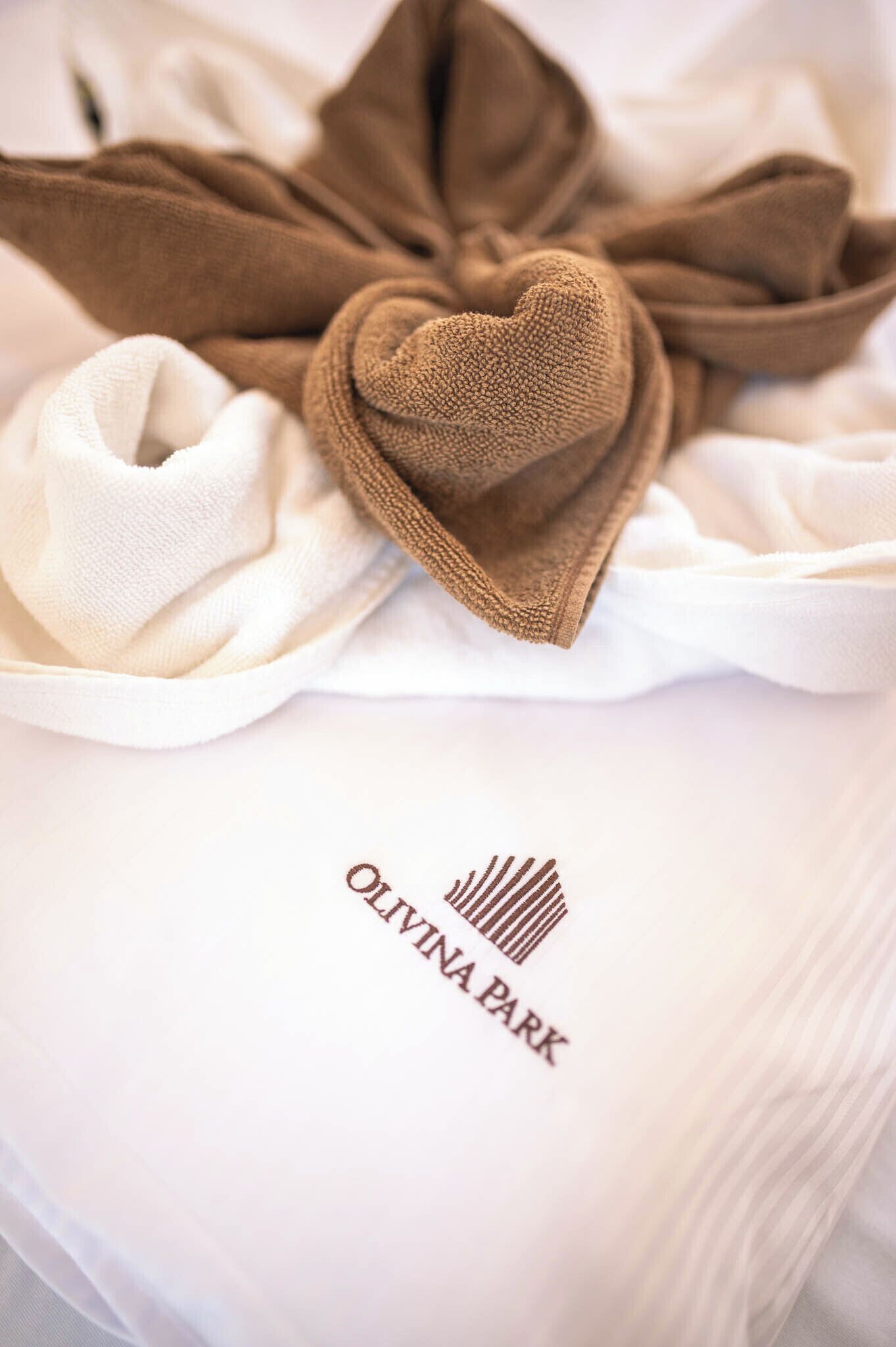A white pillow with the text "OLIVINA PARK" and a heart-shaped brown pillow on top.