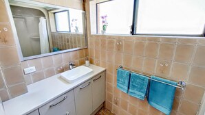 Ein Badezimmer mit einem weißen Waschbecken, einem Spiegel, einem Fenster mit Blick auf Blumen und einem Handtuchhalter mit blauen Handtüchern.