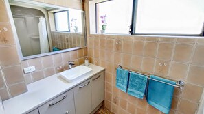 Un baño con un lavamanos blanco, un espejo, una ventana con vistas a flores y un perchero con toallas azules.