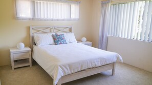 Un dormitorio con una cama, dos mesitas de noche, una lámpara de pared y una ventana con persianas.