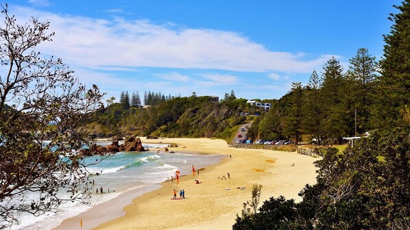 A beach with clear skies, sandy shore, and rocky outcrops.