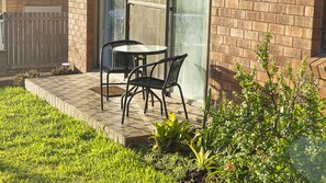 Un patio al aire libre con una mesa y sillas, un muro de ladrillo y un área verde con plantas.