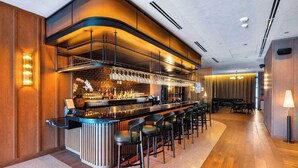 Eine moderne Bar mit einer langen Theke, mehreren Barhocker und einer Auswahl an Flaschen und Gläsern.