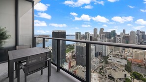 Ein Balkon mit Tisch und Stühlen, mit Blick auf eine Skyline aus Hochhäusern und ein Gewässer.