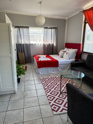 Ein Schlafzimmer mit einem Bett, einem Glastisch, einer Couch, einer Zimmerpflanze und einem gemusterten Teppich.