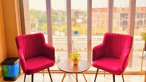 A room with two red chairs facing a window overlooking a construction site. - Hotel Pearl Grand by Elena Group (Dera Bassi)