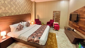 A hotel room with a large bed, a TV mounted on the wall, a wooden headboard, and a patterned wallpaper. - Hotel Pearl Grand by Elena Group (Dera Bassi)