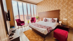 A modern bedroom with a large bed, two red armchairs, a small table, and a TV on a desk. - Hotel Pearl Grand by Elena Group (Dera Bassi)