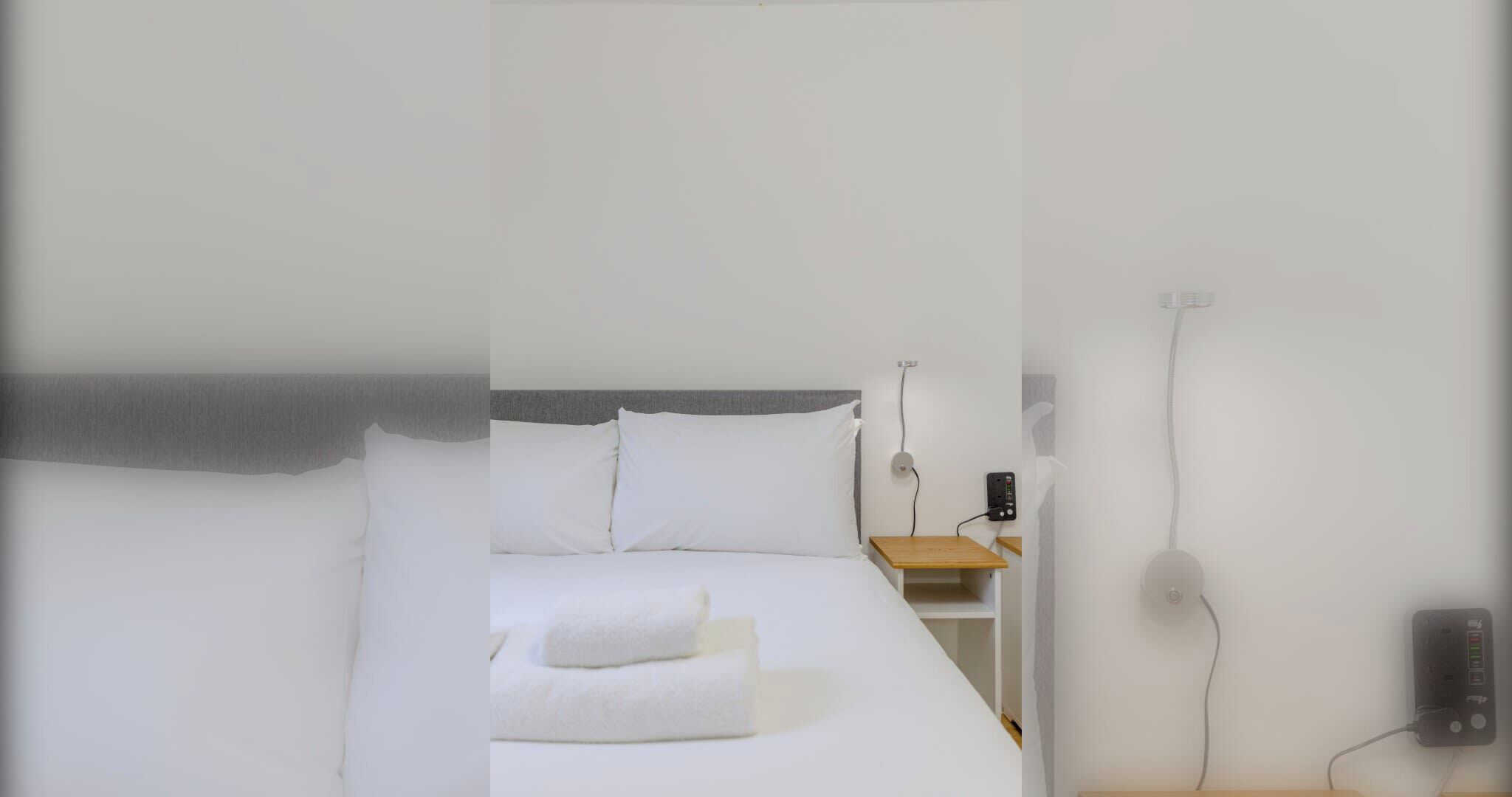 Habitación de hotel con cama, mesita de noche, lámpara y enchufe.