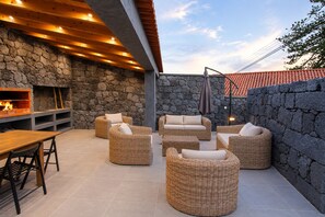 An outdoor patio with stone walls, a built-in fireplace, wicker furniture, and a tiled floor.