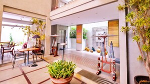 A spacious lobby with a high ceiling, a central seating area with a table and chairs, and a large potted plant in the foreground. - KoenoKoeni Boutique Hotel (Parongpong)