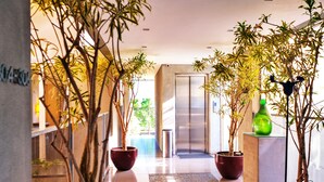 A modern hallway with potted plants, a tiled floor, and a glass elevator. - KoenoKoeni Boutique Hotel (Parongpong)