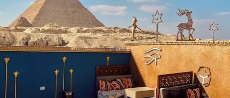 A room with a view of the pyramid, a bed, a small table, and decorative wall art.