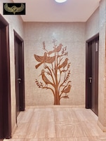 Un pasillo con un mural en la pared que muestra aves en un árbol, dos puertas y suelo de baldosas.