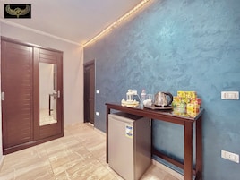 A hallway with a wooden door, a small refrigerator, a table with kitchenware, and a blue textured wall.
