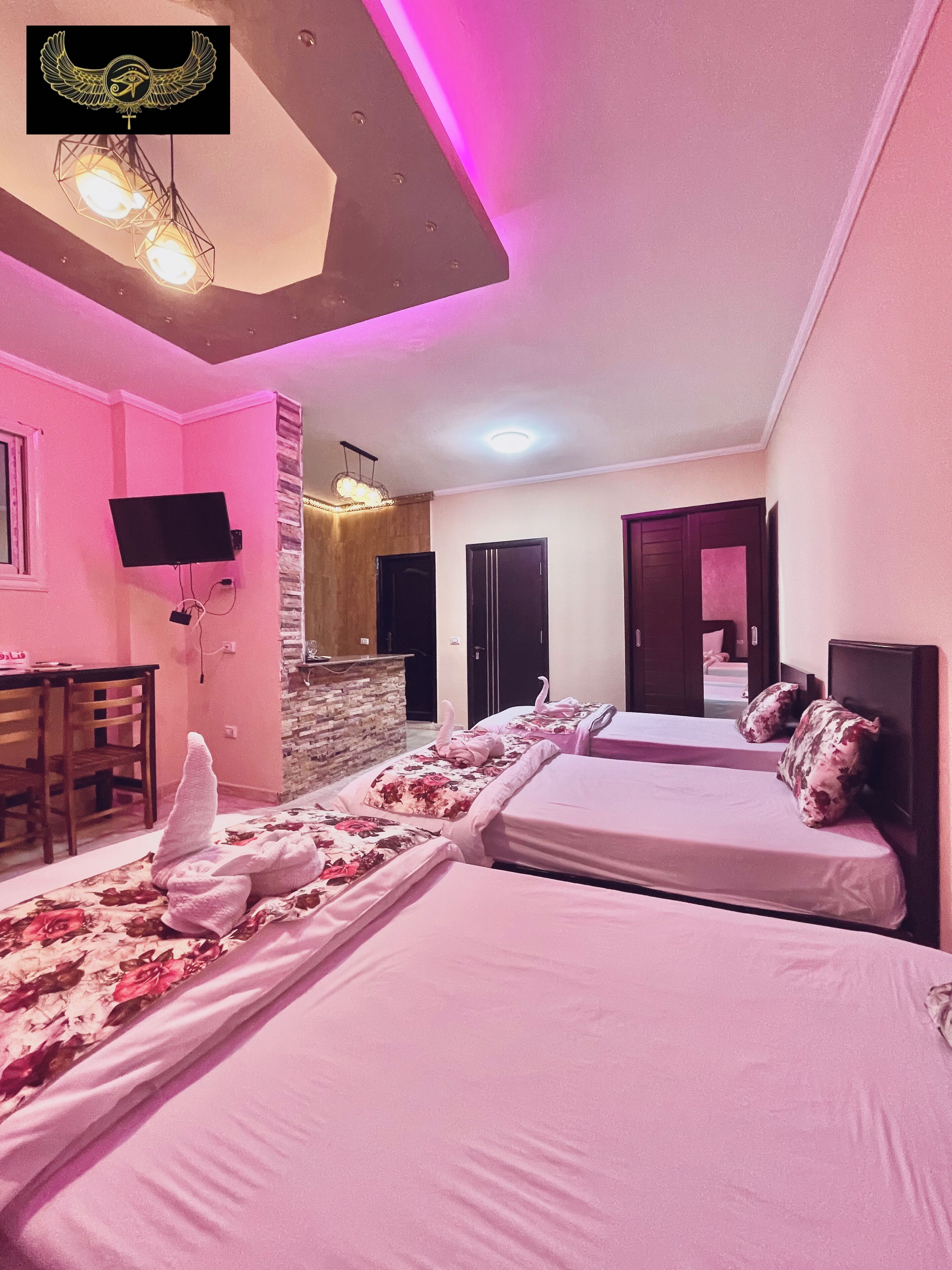 A hotel room with two beds, a desk, a TV, and a stone wall.