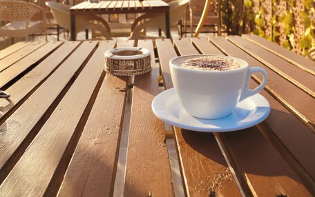A wooden table with a cup of coffee and a decorative item, set against a backdrop of pyramids and a clear sky.