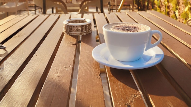 Un tavolo di legno con una tazza di caffè e un oggetto decorativo, con le piramidi e un cielo sereno sullo sfondo.