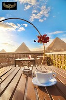 A wooden table with a cup of coffee and a decorative item, set against a backdrop of pyramids and a clear sky.